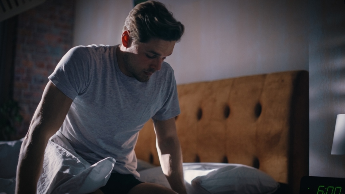 Man sitting on edge of bed looking fatigued in the morning representing low testosterone symptoms including persistent tiredness and low energy