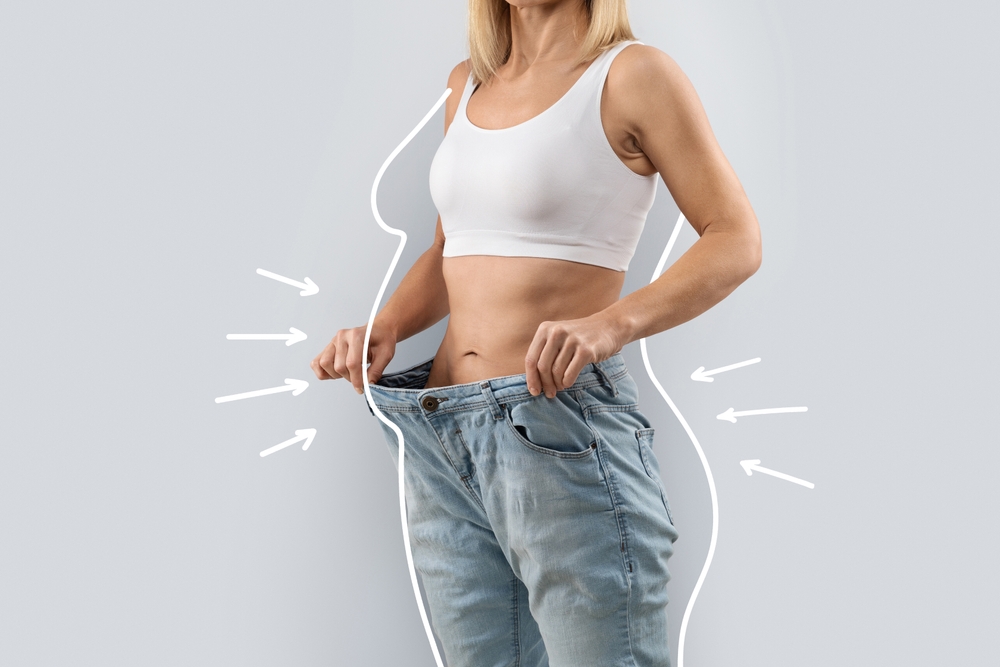 Woman pulling out the waistband of oversized jeans showing significant body transformation representing how to maintain weight loss results after a medical program