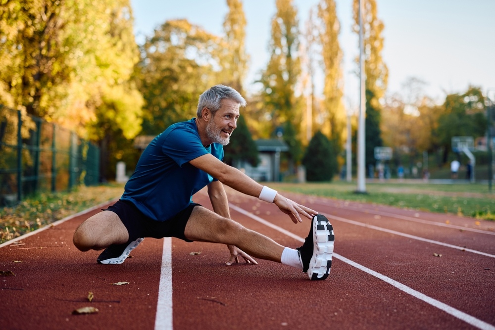 Fit middle-aged man smiling while stretching on a running track representing improved energy and physical performance along the TRT results timeline