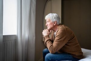 Older man sitting quietly and looking out a window representing the question of low testosterone vs aging and unexplained mood and energy changes