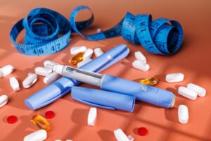 Blue injection pens and weight loss pills with a measuring tape representing the comparison between semaglutide vs tirzepatide as prescription weight loss medications