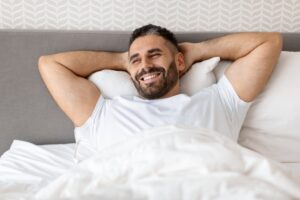 Man smiling and relaxed in bed with hands behind his head representing improved wellbeing and the importance of understanding TRT and fertility before starting testosterone therapy