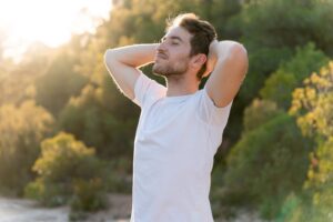 Young man standing outdoors with eyes closed and hands behind his head looking relaxed and energized representing improved wellbeing when estrogen levels in men on TRT are properly balanced