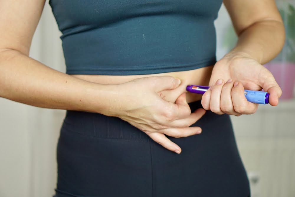 Woman in athletic wear self-administering a semaglutide injection into her abdomen representing continued treatment during a weight loss plateau on semaglutide
