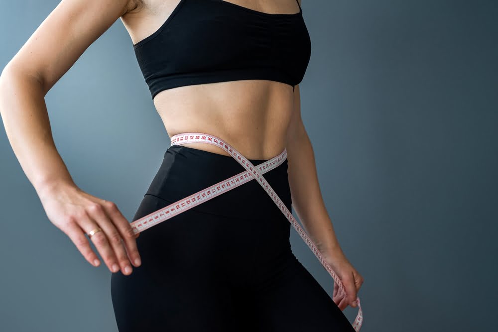 Woman measuring her waist to track progress on a medical weight loss in Arizona telehealth program with Invite Wellness