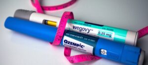 Wegovy and Ozempic semaglutide injection pens side by side wrapped in a pink measuring tape representing the comparison of Ozempic vs Wegovy for weight loss and diabetes treatment