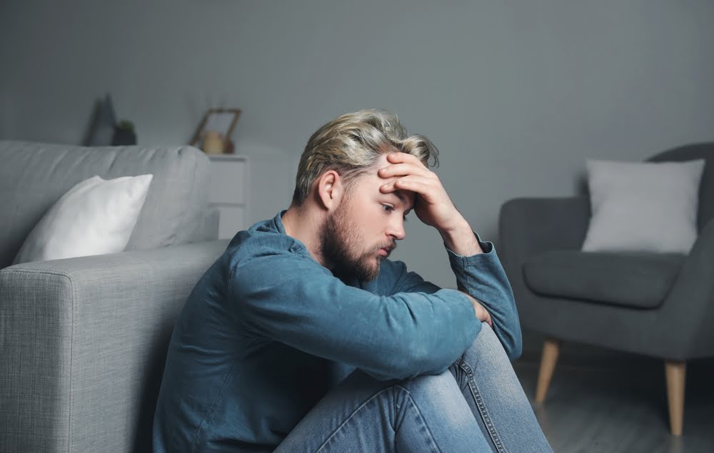 Man sitting alone on the floor with his head in his hand and knees pulled to his chest representing the emotional weight of testosterone and depression in men with low hormone levels