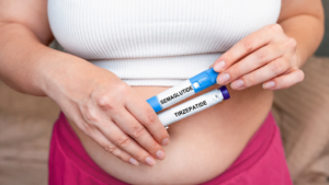Person holding labeled semaglutide and tirzepatide injection pens near their abdomen representing the comparison of tirzepatide side effects against semaglutide during medical weight loss treatment