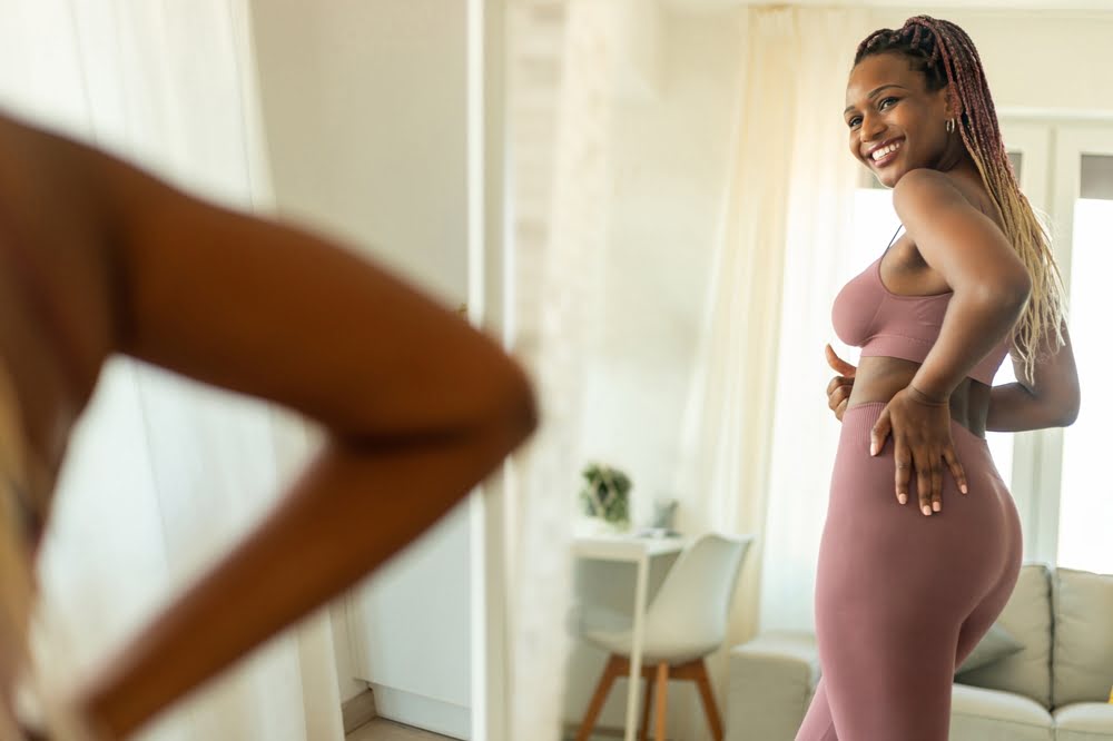 Confident woman smiling at her reflection in the mirror after achieving results through a medical weight loss in New Mexico telehealth program with Invite Wellness